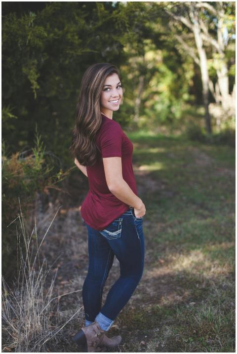 A young woman with long hair smiles outdoors in a