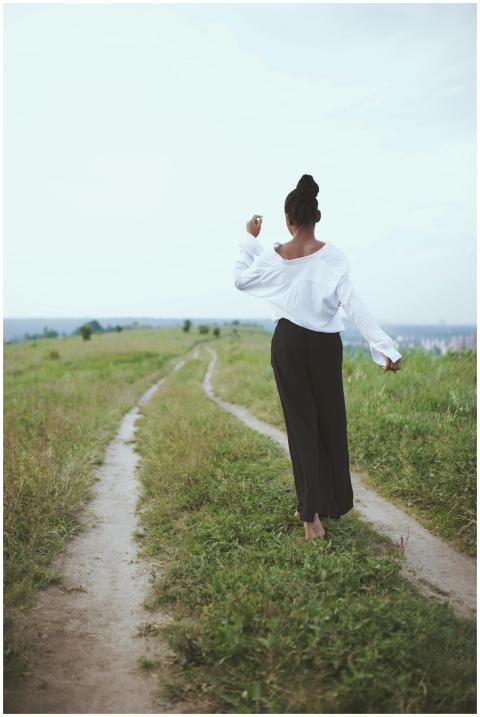 A woman walks barefoot on a grassy rural path, emb