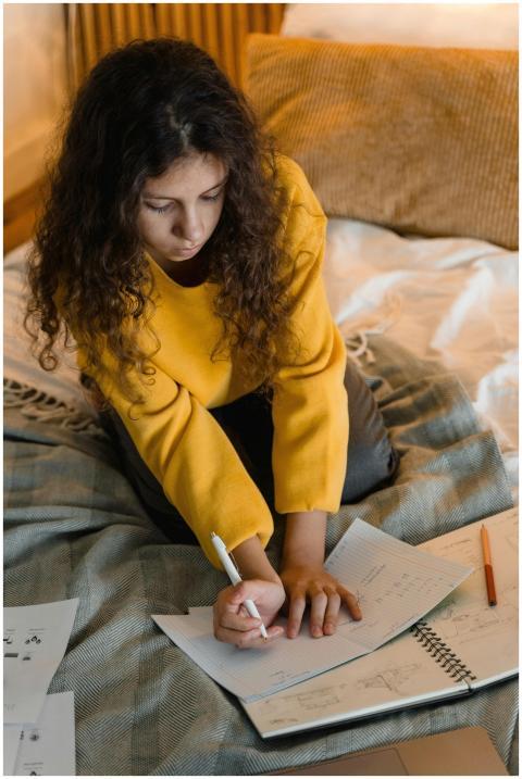 Young girl in yellow sweater writing on a notebook