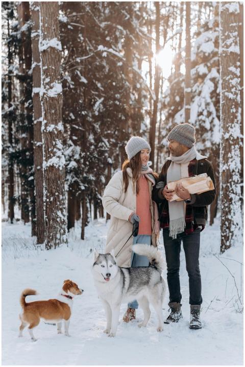 Happy couple walking with dogs in snowy forest, en