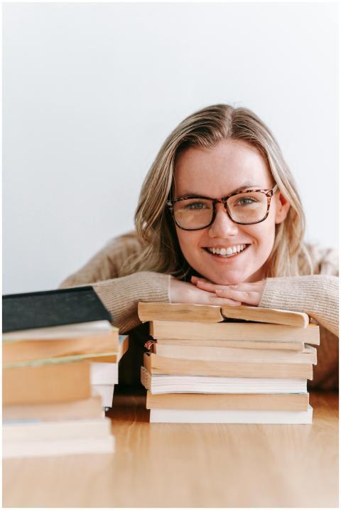Caucasian woman leaning on a stack of books, smili