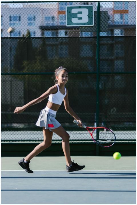 A young girl in activewear playing tennis outdoors