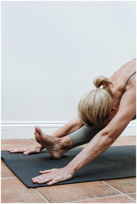 Adult woman stretching on yoga mat indoors, promot