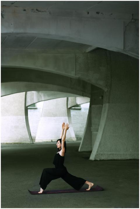 A woman performs yoga poses under a modern bridge