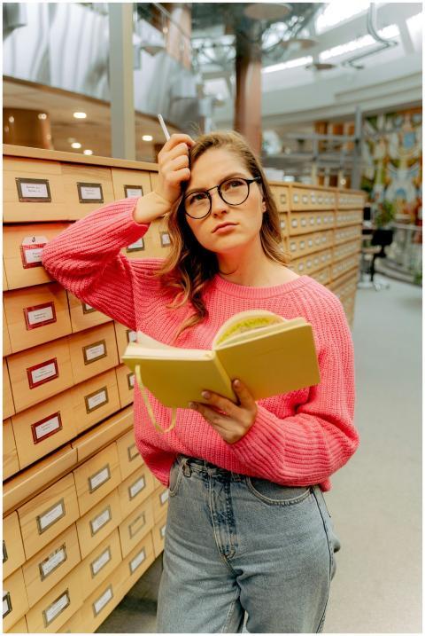 Young woman in glasses reading a book in a library