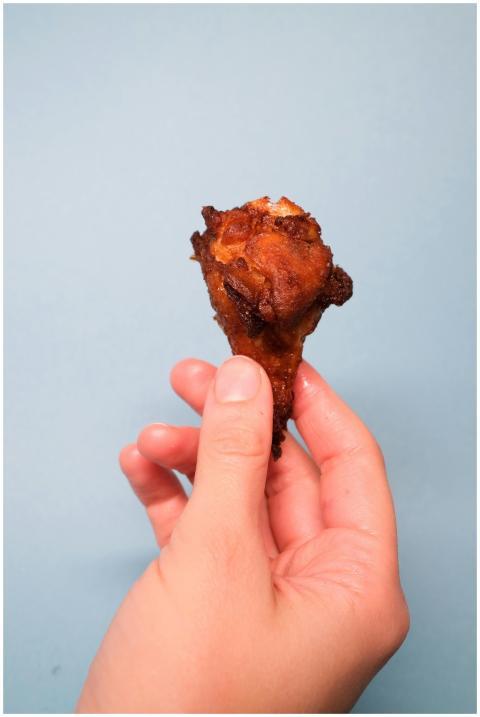 Close-up of a crispy fried chicken drumstick held