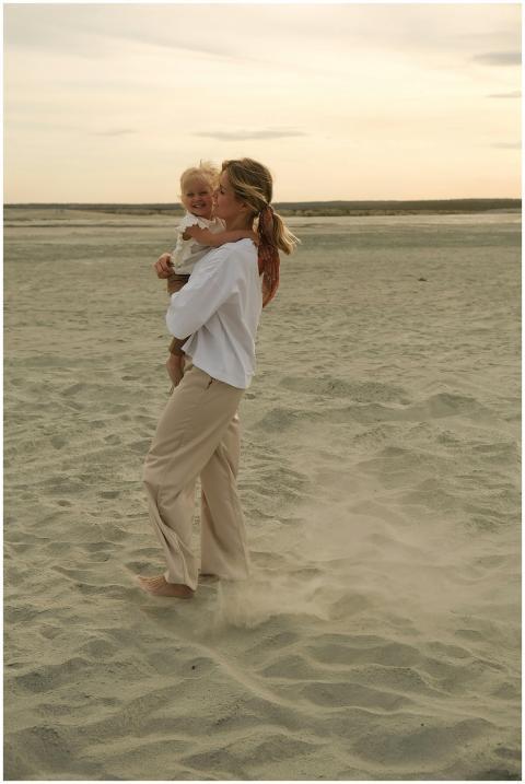 A mother and baby walking on a sandy beach during