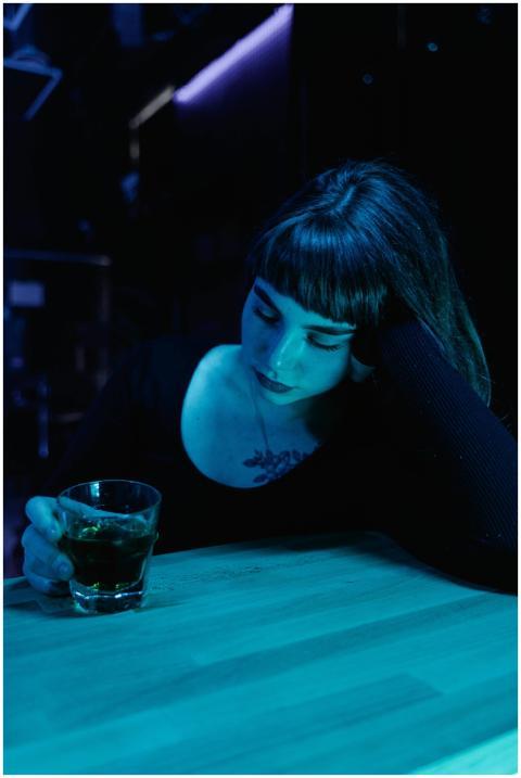 A woman ponders over a drink in a moody, neon-lit