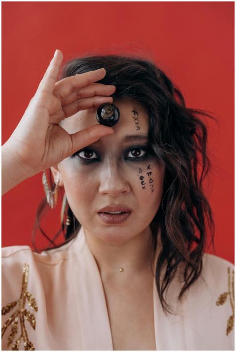 A woman holds a crystal sphere over her eye agains