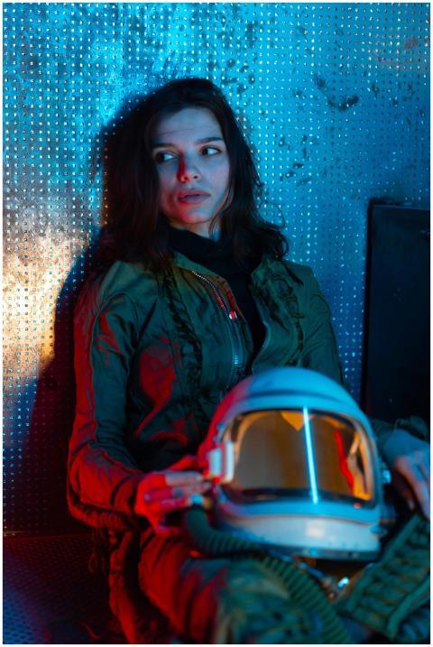 A spacewoman in a futuristic suit rests against a