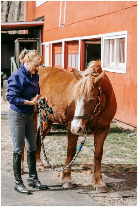 Woman holding a horse lead outside a rustic red ba