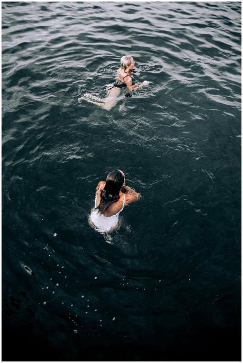Two women swim in deep blue water, captured from a