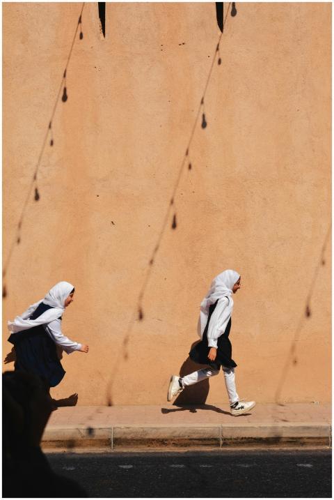 Two young girls run energetically past a sun-dappl
