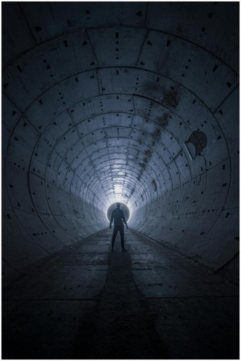A silhouetted man stands in a dark tunnel, evoking