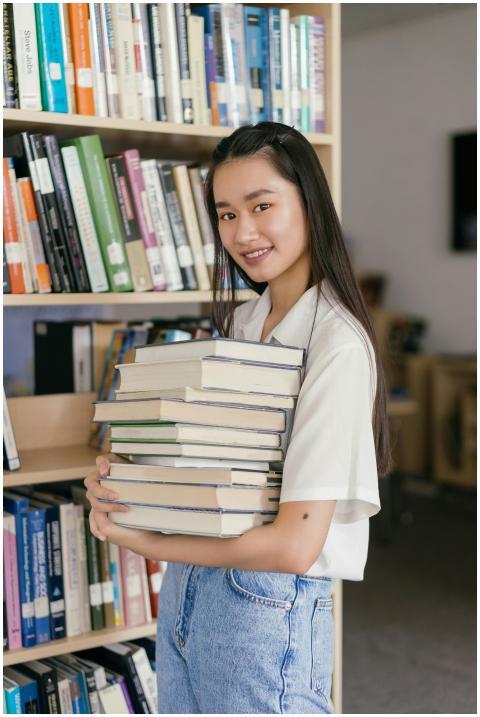 Asian female student in a library, smiling and hol