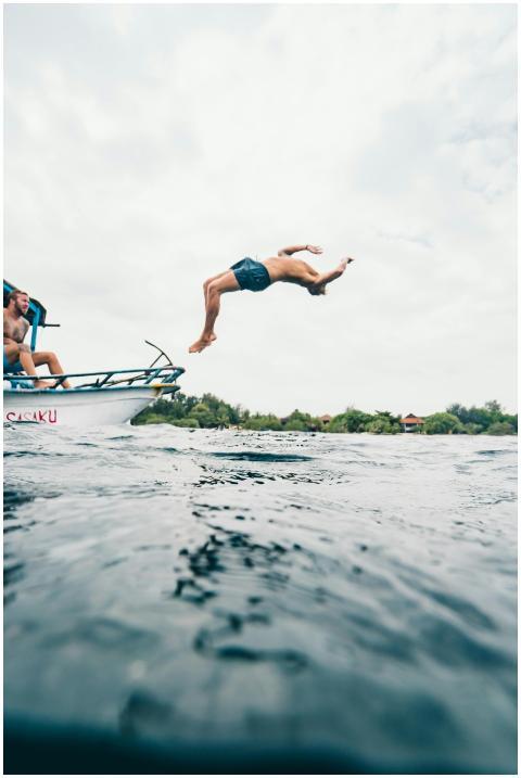 A man performs a backflip dive into the ocean from