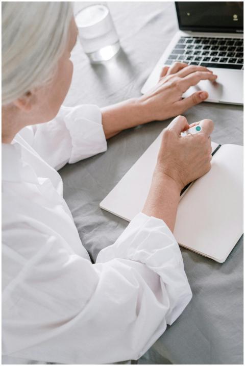Elderly woman takes notes while using a laptop at