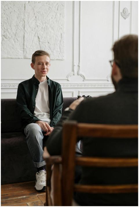 A teenager sits across from a counselor in a thera