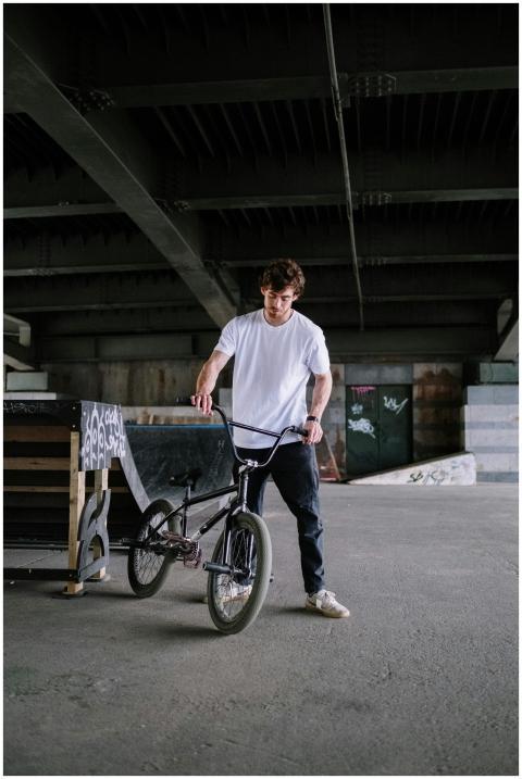 A man in a white t-shirt holds a BMX bike under a