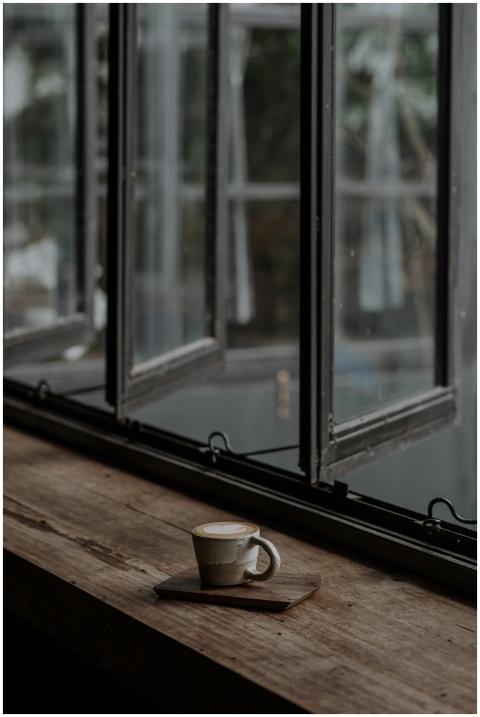 A warm coffee mug sits on a rustic wooden windowsi