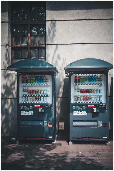 Two vending machines outdoors against a wall, offe