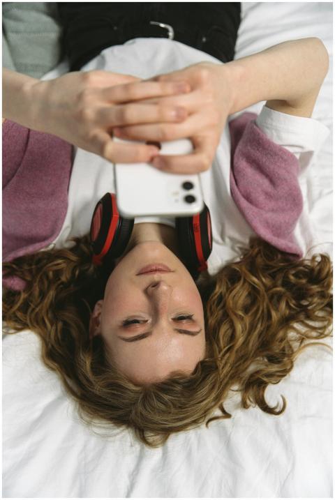 Young woman lying on bed using smartphone, wearing