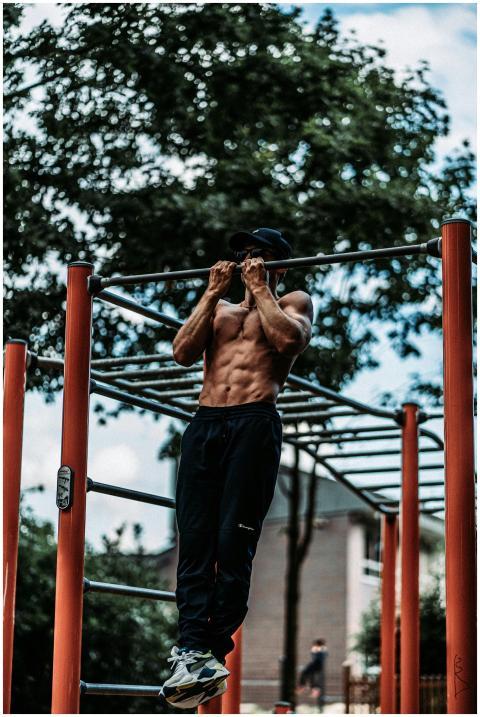 Athletic man performing pull-ups on a bar outdoors