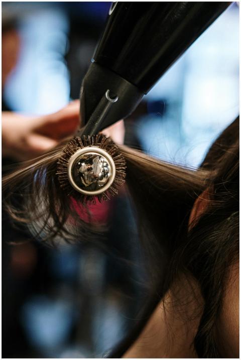 Close-up of a hairstylist styling hair with a brus