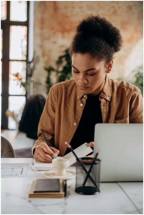 Woman taking notes at a desk with a laptop, focusi