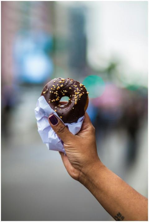 A person holds a chocolate glazed donut with sprin