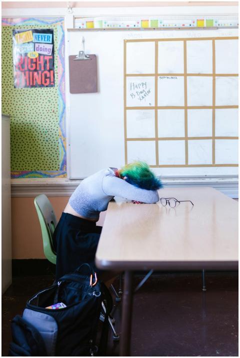 Student resting on desk in a colorful classroom, d