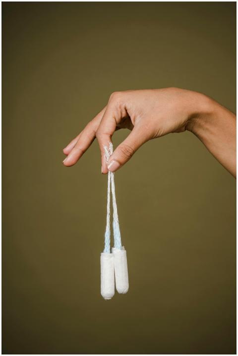 A woman's hand holding two tampons against an oliv