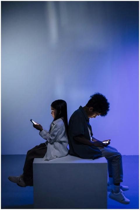 Children sitting back to back using smartphones, i