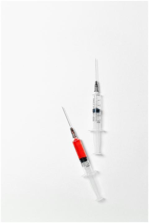 Close-up of syringes filled with red liquid on a w