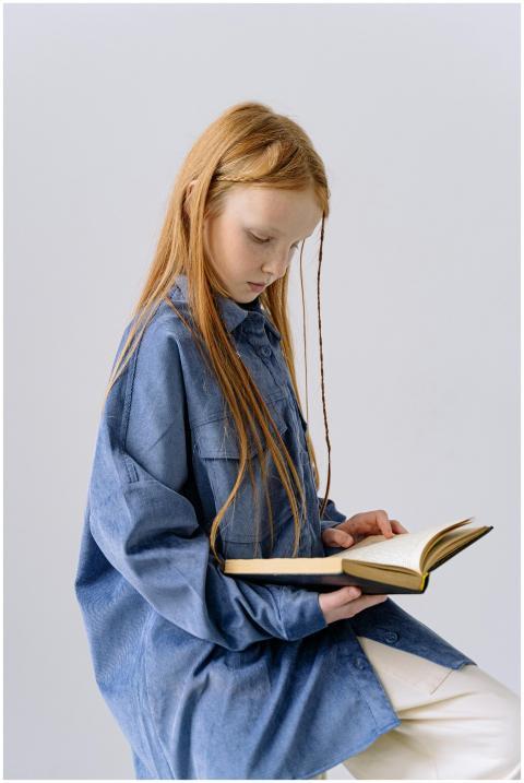 A young girl with long blonde hair reads a book, d