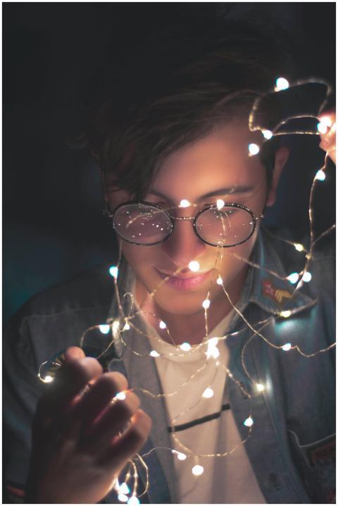 Young man with glasses illuminated by fairy lights