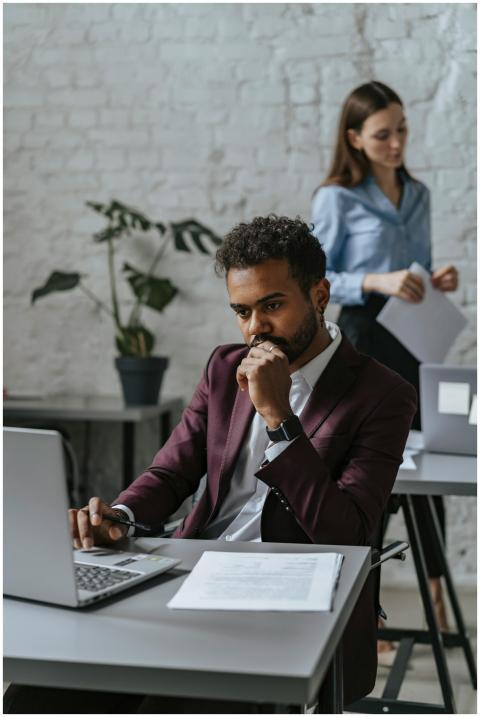 Pensive man using laptop in modern office with fem