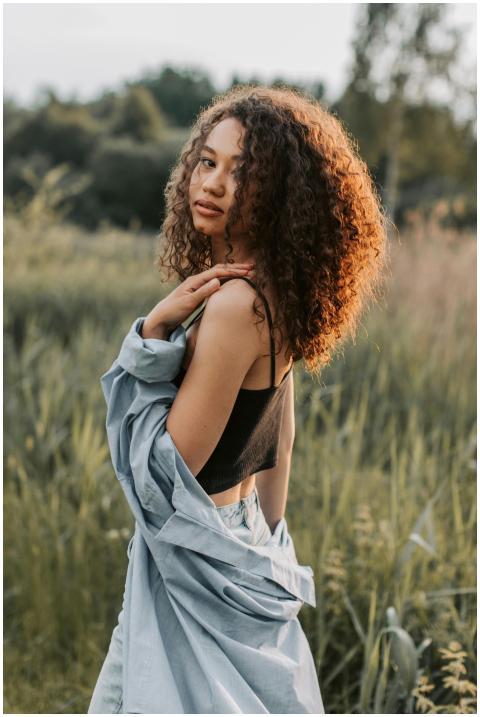 Stylish woman with curly hair posing in a field, e