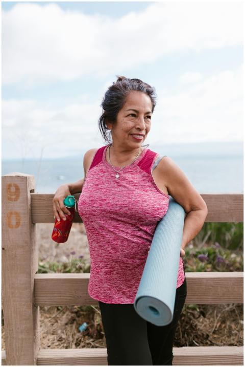 Smiling senior woman holding yoga mat outdoors by