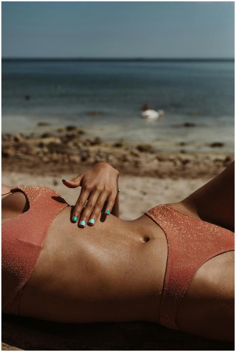 A woman sunbathes on a sandy beach wearing a glitt