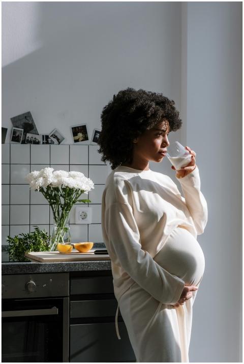 Pregnant woman drinking milk in a sunlit kitchen,