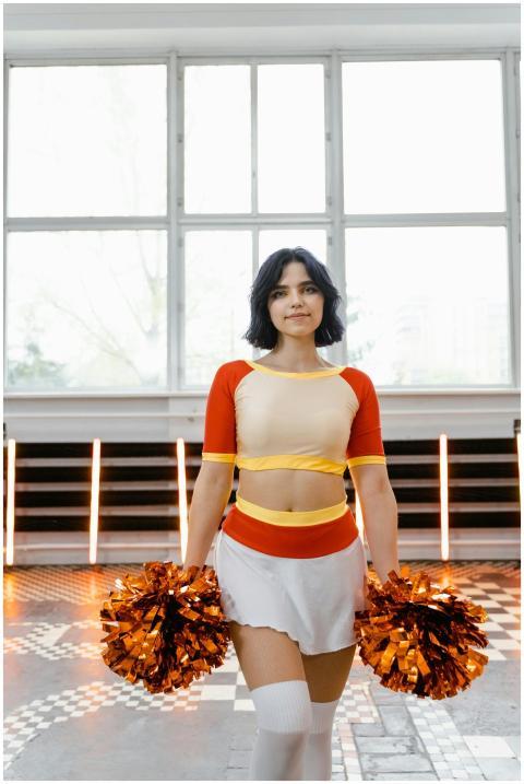A young cheerleader posing indoors holding orange