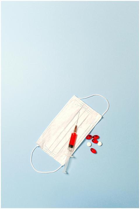 Flat lay of face mask, syringe, and pills on a blu
