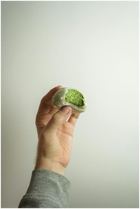 A hand holding a partially eaten green matcha moch