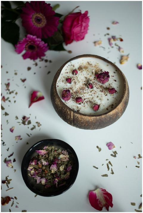 A cozy candle surrounded by rose petals and herbs