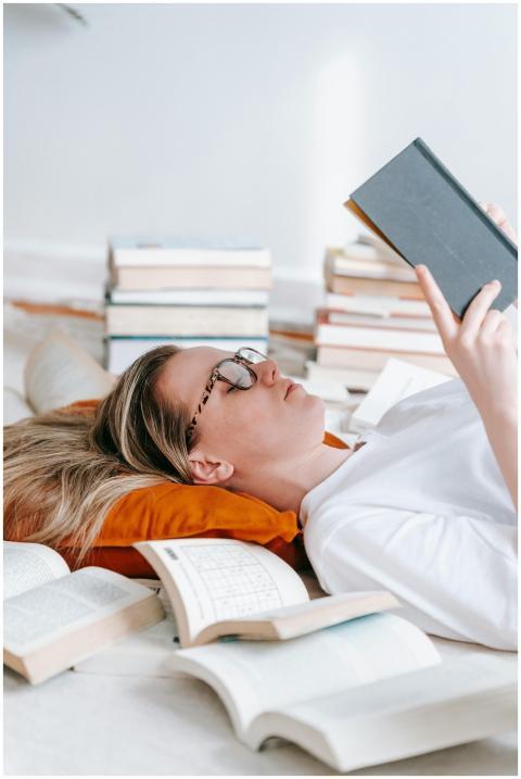 A young woman lies on pillows, engrossed in a book