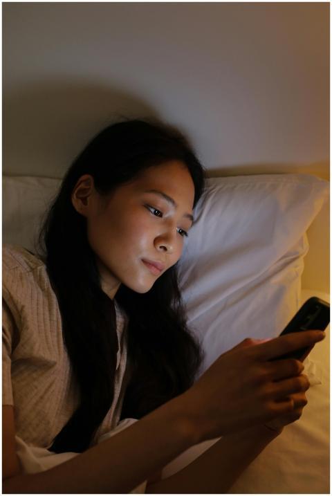 Asian woman relaxing in bed using smartphone durin
