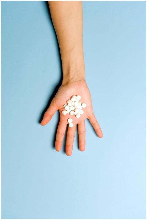 A hand holding white pills on a light blue backgro