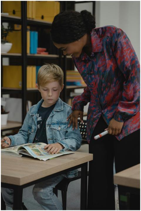 A teacher guides a student reading a book in a cla