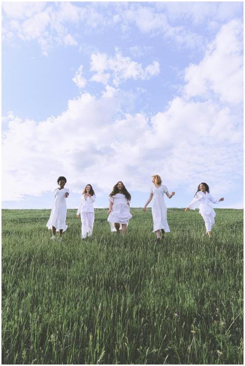 Five diverse women in white dresses running joyful